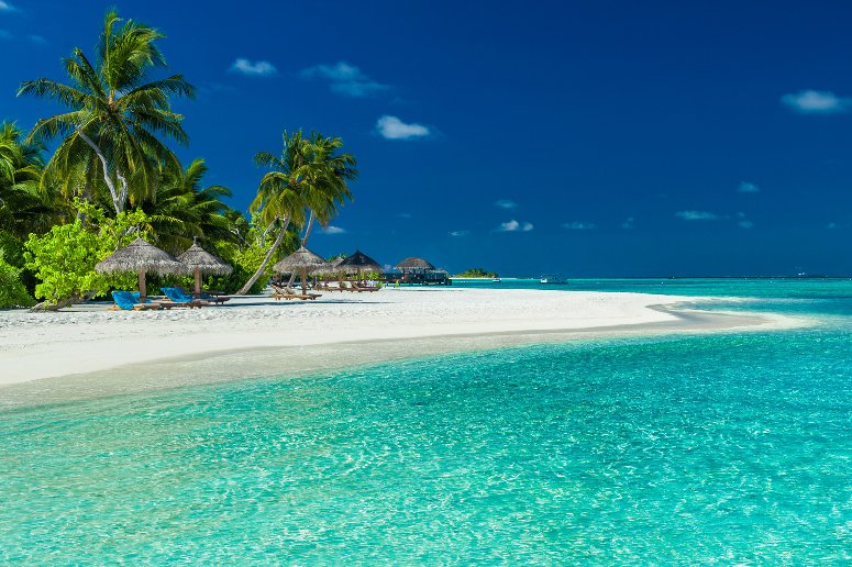 Palm trees and beach umbrelllas over lagoon and white sandy beach, Maldives island
